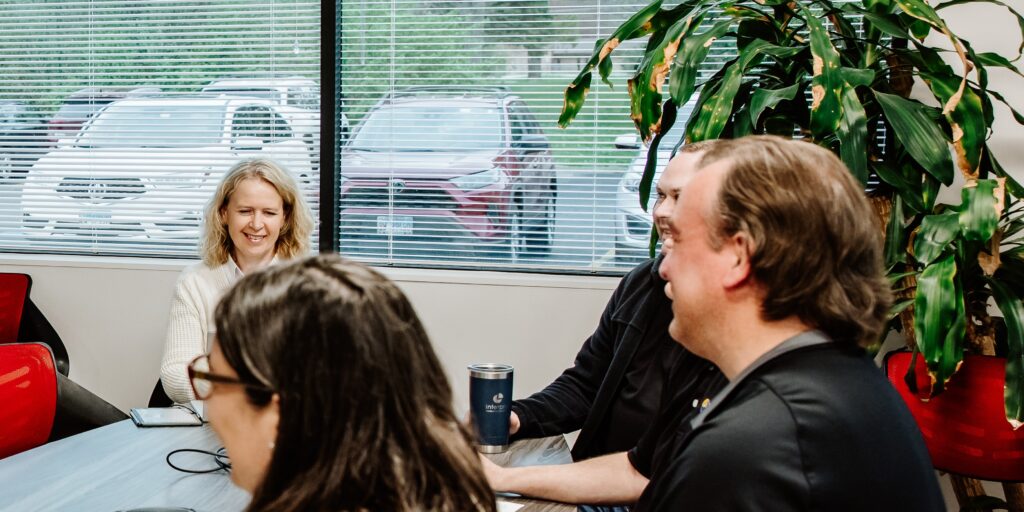 Sam Somerville, Justin Carrell, Larry Pilotto, and Arianna Martin seated around a table in an office meeting room, engaged in discussion.