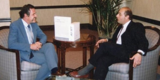 John Greenwood and Ralph Strozza seated in armchairs, engaged in a professional conversation around a small table.