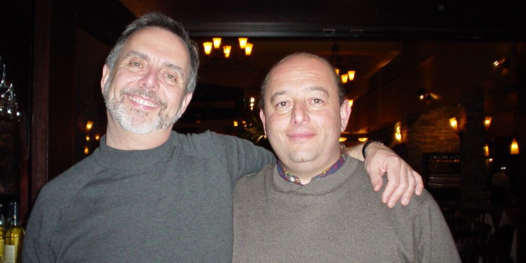 Mack Campbell and Ralph Strozza standing together indoors with arms around each other, smiling.