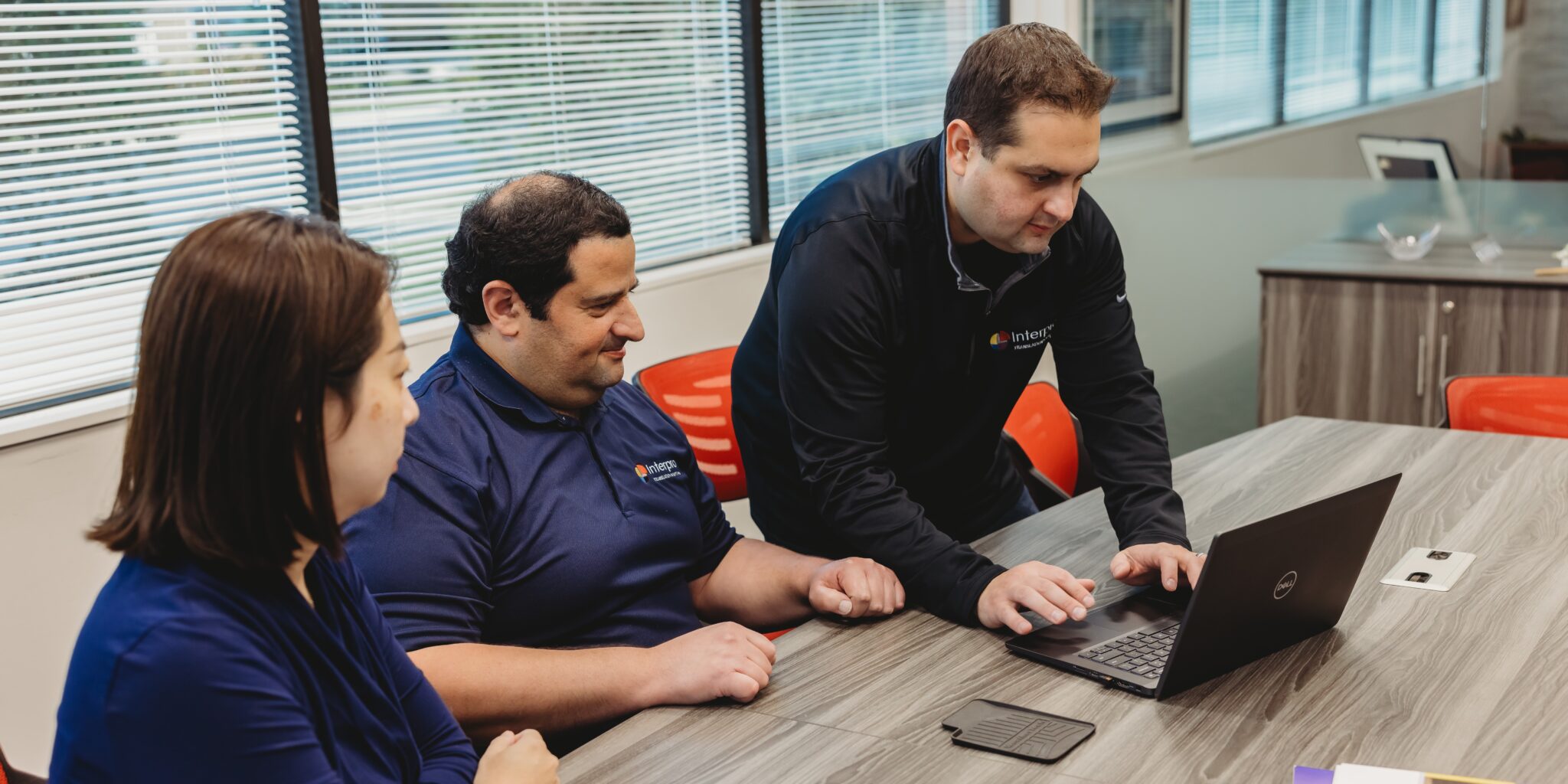 Three Interpro team members review AI Translation Post-Editing workflows around a laptop in a modern office environment