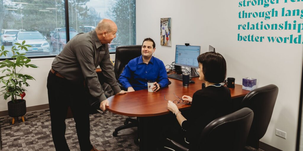 Three Interpro team members in an office setting discussing a Translation Quality Estimation project around a wooden desk.