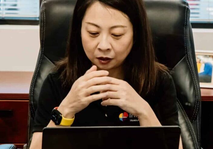 Interpro Team Coordinating Professional Interpreting Services Interpro Chinese team member sitting at desk coordinating professional translation services from laptop.